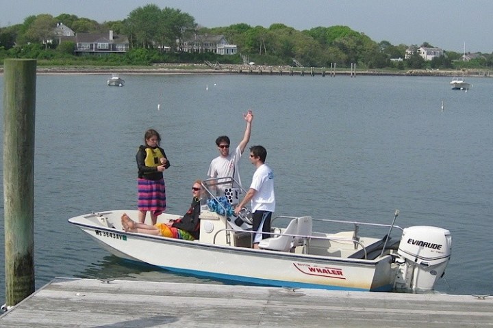 Four people enjoying a small motorboat by a dock on a calm lake.