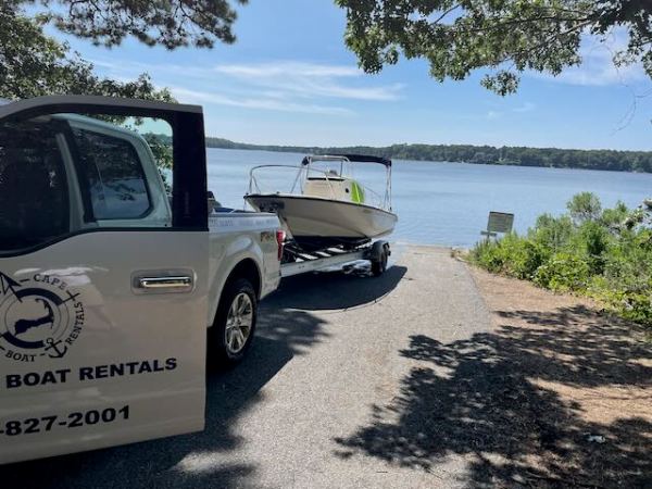 Truck towing a boat on a trailer near a calm lake under a clear sky.